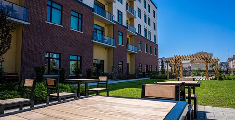 Residence facade beside patio tables, lawn and a pergola.