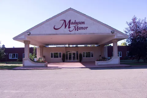 Building entrance with a large canopy, glass doors, columns and planted beds