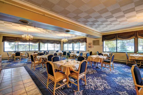 Dining room with set tables, blue chairs, chandeliers and windows overlooking the water.