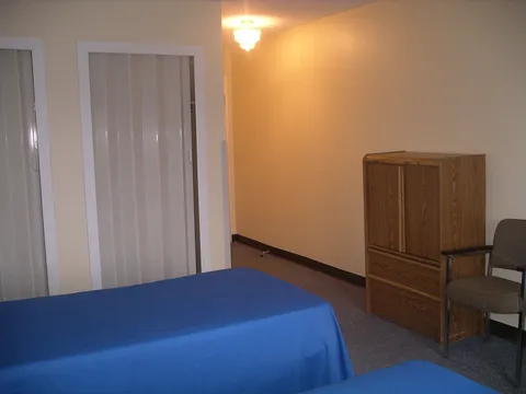 Bedroom with a single bed, wooden drawers and a curtained window.