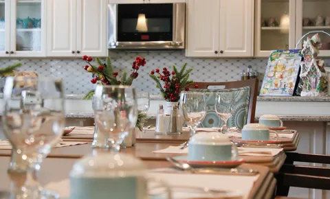 Dining table set beside a kitchenette and flower arrangements.