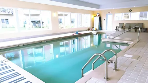 Indoor pool with steps, handrails, chairs and large windows