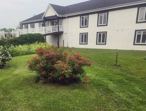 White residence exterior beside a green lawn and flowering red shrubs