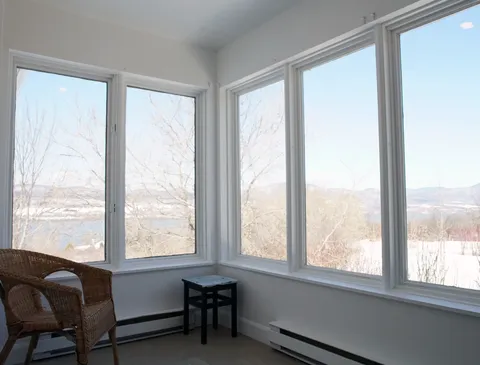 Wicker chair and side table beside tall windows overlooking a river