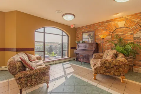 Sitting area with patterned chairs, a piano and stone wall.