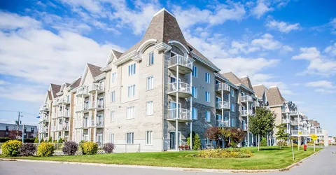 Residence building with pitched roofs and balconies beside a lawn.