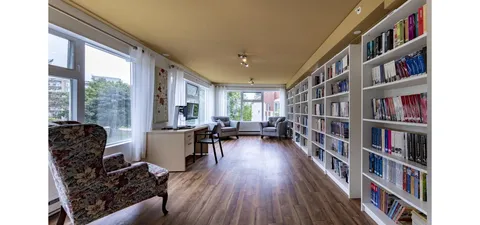 Library with bookcases, tables and armchairs beside windows.