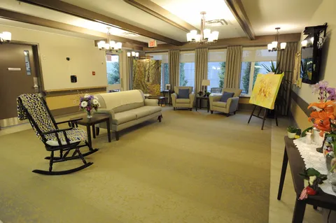 Room with a sofa, armchairs, a rocking chair and an easel beside the windows