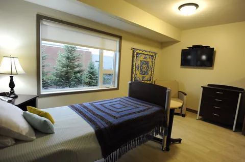 Bedroom with a bed, a television and a colourful quilt on the wall