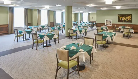 Dining room with tables set with green cloths, chairs and tall windows.