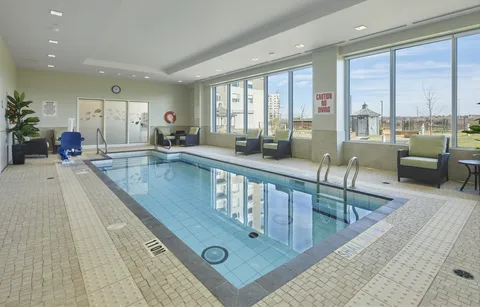 Indoor pool with a pool lift, handrails, chairs and large windows.