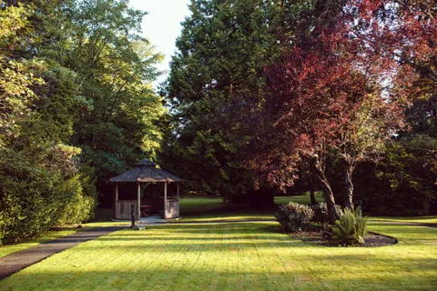 Lawn and garden paths leading to a gazebo beneath mature trees.