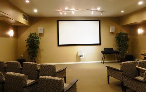 Screening room with upholstered chairs, a blank projection screen and potted trees.