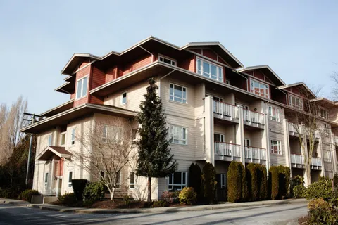 Corner view of the residence with gabled roofs, balconies and shrubs.