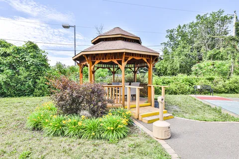 Garden gazebo beside shrubs, flowers and a paved path