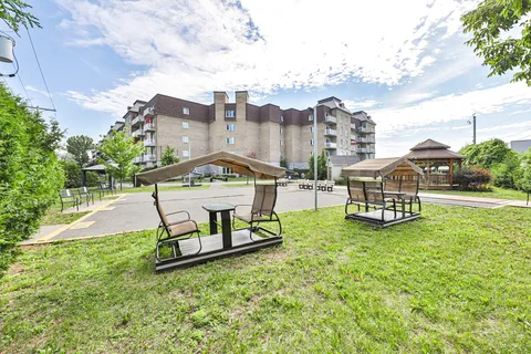 Residence exterior beyond a lawn with covered swings and paved paths