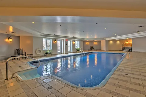 Indoor swimming pool with handrails, chairs and a tiled deck