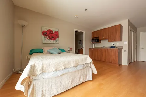Bedroom with a white bedspread, flower artwork and a wooden kitchenette