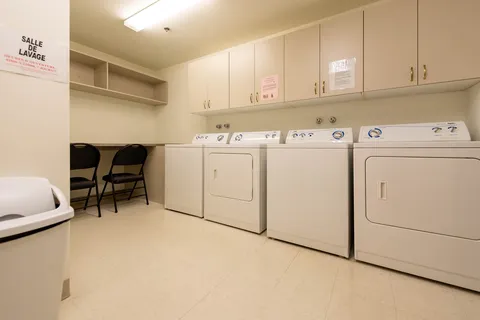 Laundry room with white dryers, overhead cabinets and folding chairs