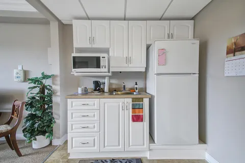 Kitchenette with white cupboards, refrigerator, microwave and a small sink