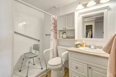 Bathroom with a vanity, toilet, grab rails and a shower chair