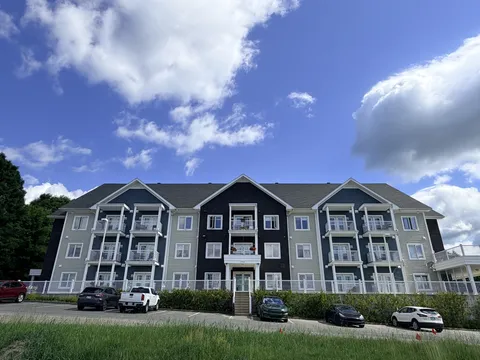 Three-storey residence with balconies and parked cars beside a lawn.