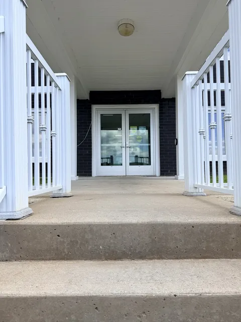 Covered entrance with steps, white railings and double glass doors.
