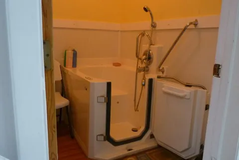 Walk-in bathtub with grab rails and a handheld shower.