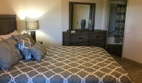 Bedroom with a patterned duvet, dresser, mirror and bedside lamp