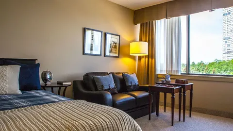 Bedroom with a bed, sofa and side table beside a large window.