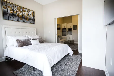 Bedroom with a white bedspread, tree artwork and an adjoining kitchenette