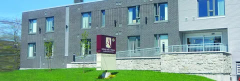 Long grey brick building beside a lawn, with windows, balconies and entrance signage