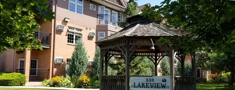 Wooden gazebo beside a brick residence, shrubs and flower beds.