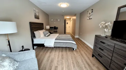 Suite bedroom with a bed, dresser, armchair and television.