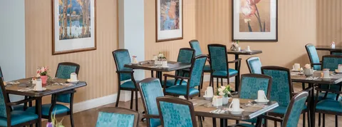 Dining room with set tables and turquoise upholstered chairs.