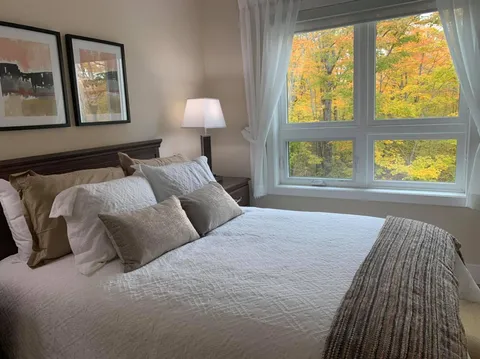 Bedroom with a double bed, table lamp and large window overlooking trees