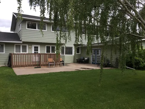 Rear of the residence with a patio and lawn beneath a willow tree.