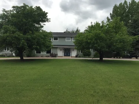 Front of the two-storey residence behind a lawn and mature trees.