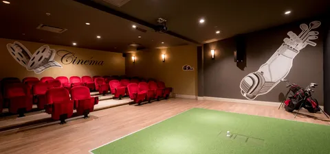Room with rows of red cinema seats and a golf practice mat