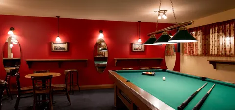 Billiards room with a green pool table, red walls and oval mirrors