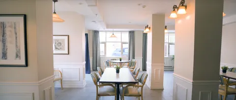 Dining tables and wooden chairs between columns beside curtained windows