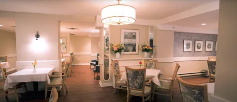 Dining room with tables, floral-upholstered chairs, mirrors, flowers and a large pendant light