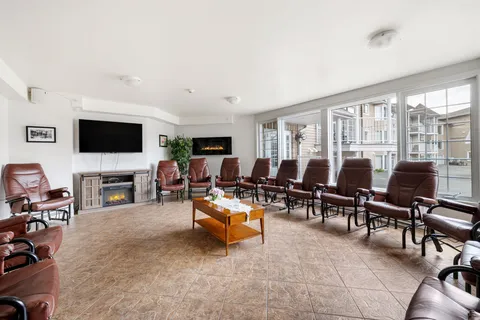 Lounge with brown armchairs, a television and windows facing the courtyard.