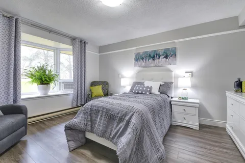 Bedroom with a grey bedspread, armchair, white dresser and window