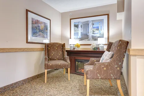 Two patterned armchairs beside a fireplace and framed landscapes
