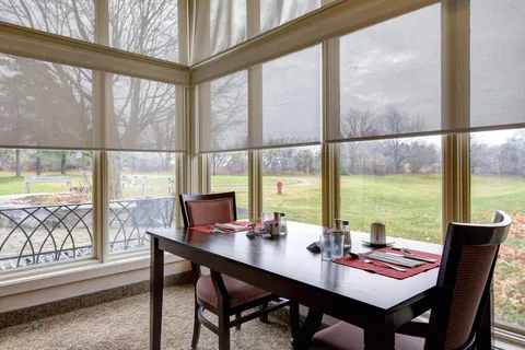 Set dining table and wooden chairs beside tall corner windows