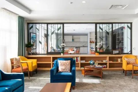 Lounge with blue and yellow seating beside broad windows.