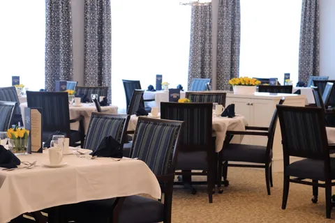 Dining room with striped chairs, set tables, white cloths and yellow flowers