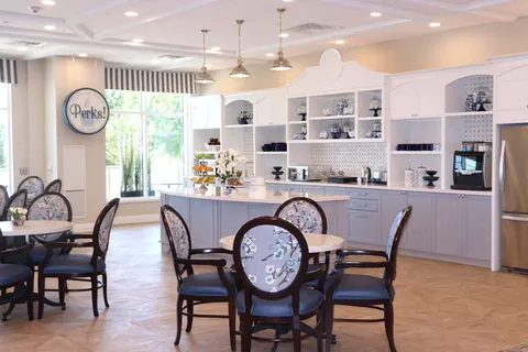 Cafe with round tables, floral chairs, a counter and shelves of crockery