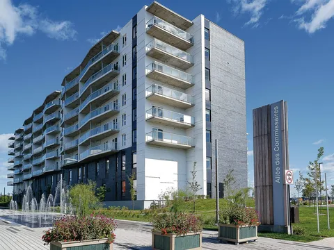 Residence with glass balconies beside a fountain, flower planters and a paved promenade